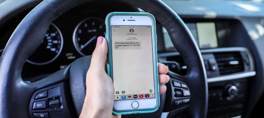 person holding up phone to car steering wheel while they review cellgate app access control notifications