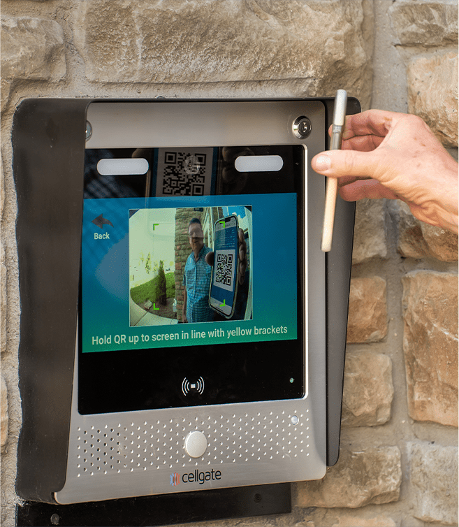 Person scanning QR code on CellGate Watchman WXL touchscreen mounted on stone wall