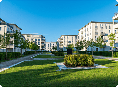 Modern multi-family residential complex courtyard with landscaped green space, walking paths, and apartment buildings
