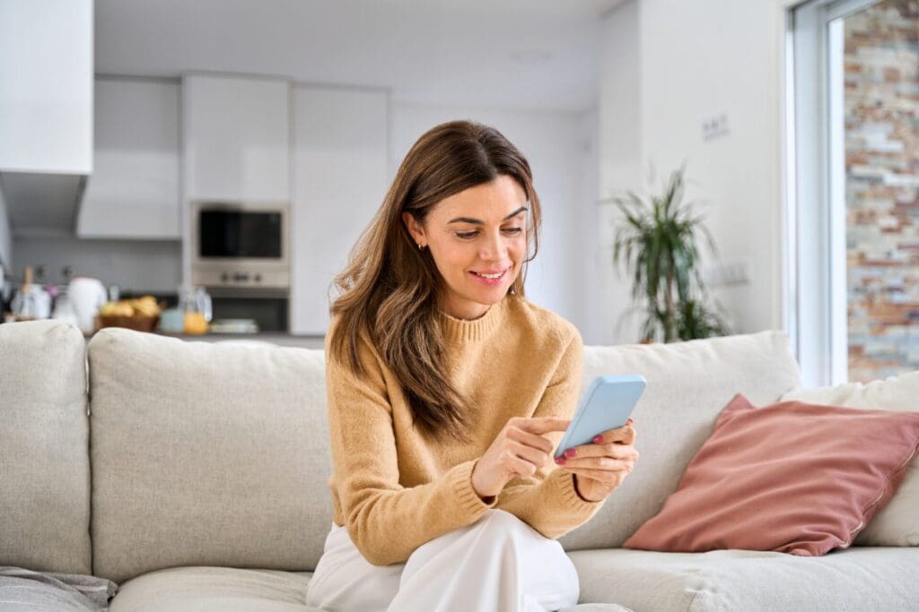 Woman sitting on a couch using smartphone inside a home